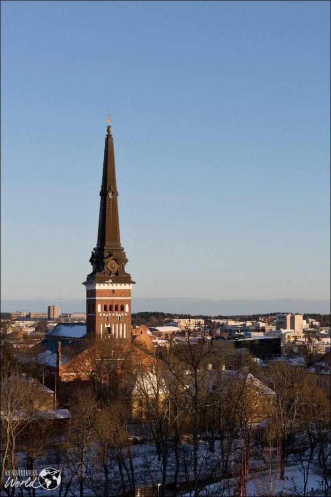 Historic church tower in Stockholm during winter with snow-covered trees.